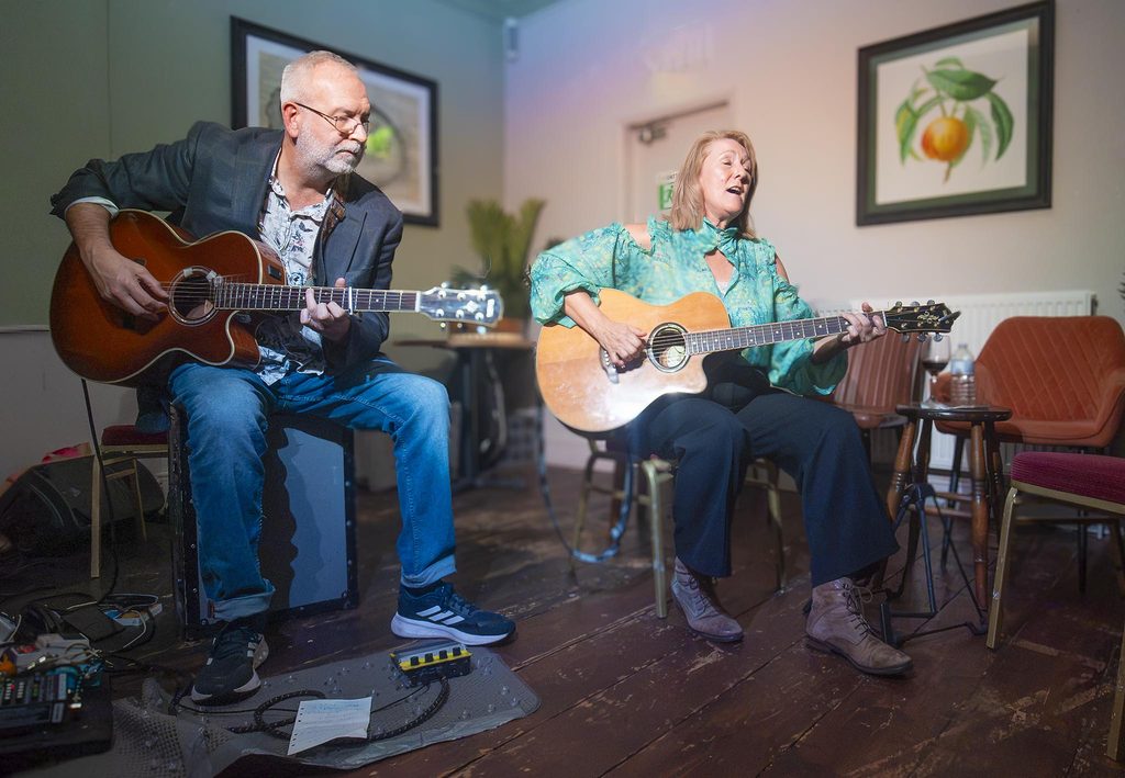 Virginia and John Kettle playing guitars. Virginia is singing.